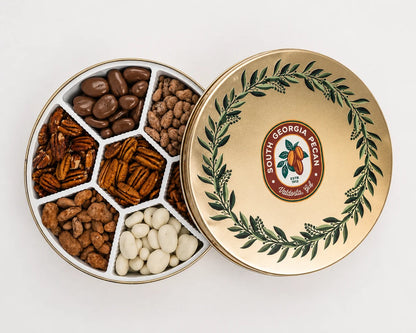 An open round tin of assorted nuts and chocolate-covered pieces, shown next to its lid. The lid is gold with a green laurel wreath and a South Georgia Pecan logo.